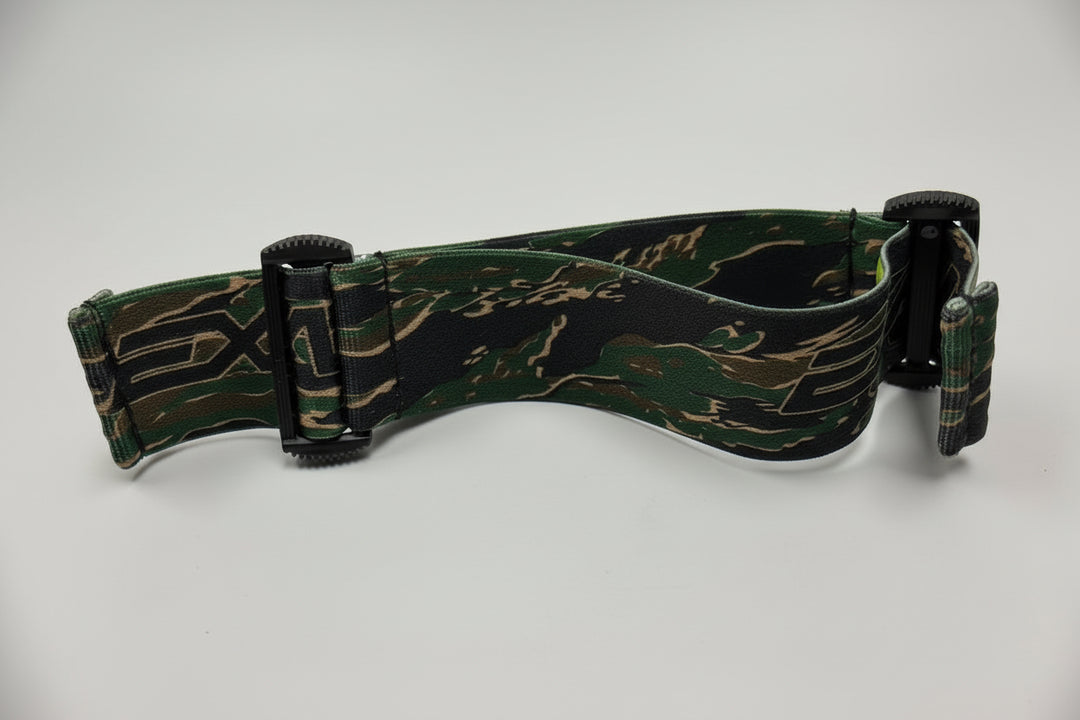 Green camouflage-patterned goggle strap on a white surface with a gray background