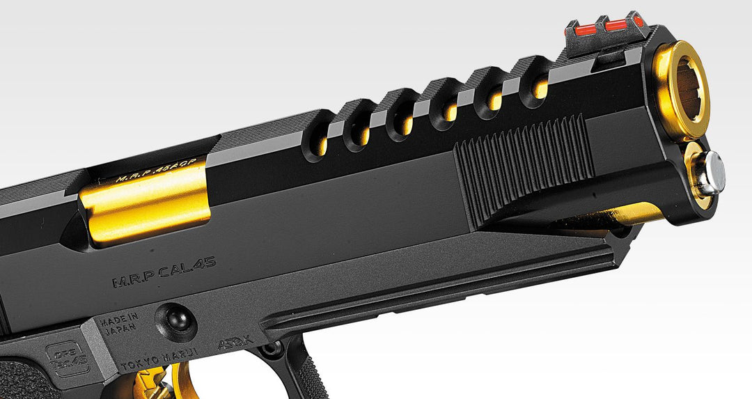 Close-up of a black and gold tactical-style firearm or prop blaster, showing the slide, rear sight, barrel tip, and textured grip against a light gray background.